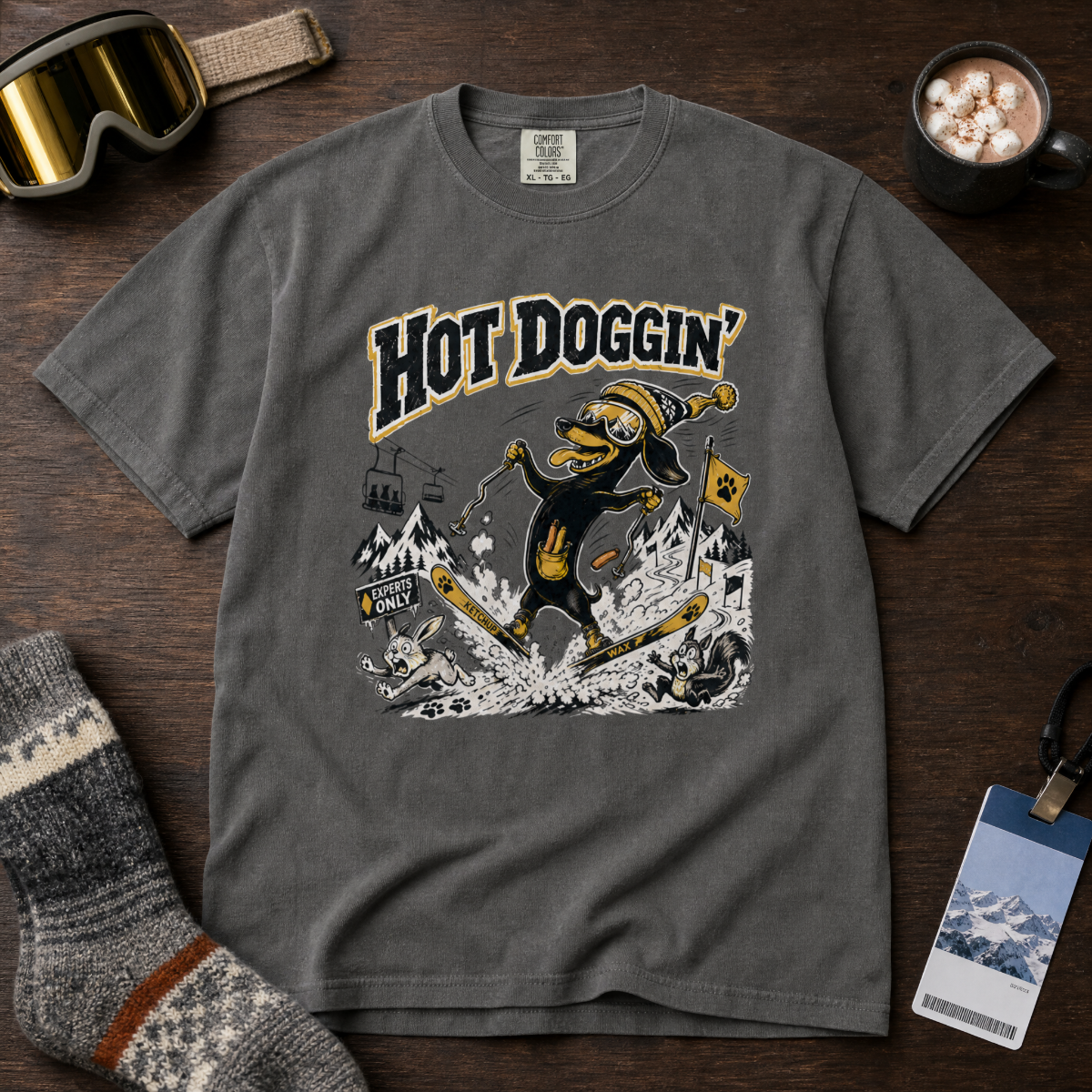 Gray t-shirt with 'Hot Doggin' graphic design on a wooden surface with accessories.