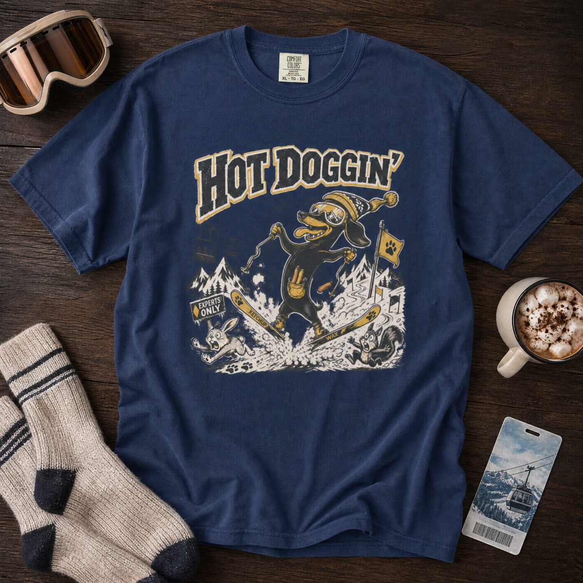 Blue t-shirt with 'Hot Doggin' graphic design on a wooden surface with accessories.