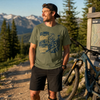 Man standing with a mountain bike in a forested area with mountains in the background