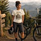 Woman standing next to a mountain bike in a forested area with mountains in the background