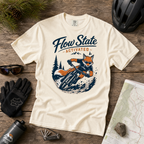 White t-shirt with 'Flow State Activated' graphic on a wooden surface with outdoor gear.
