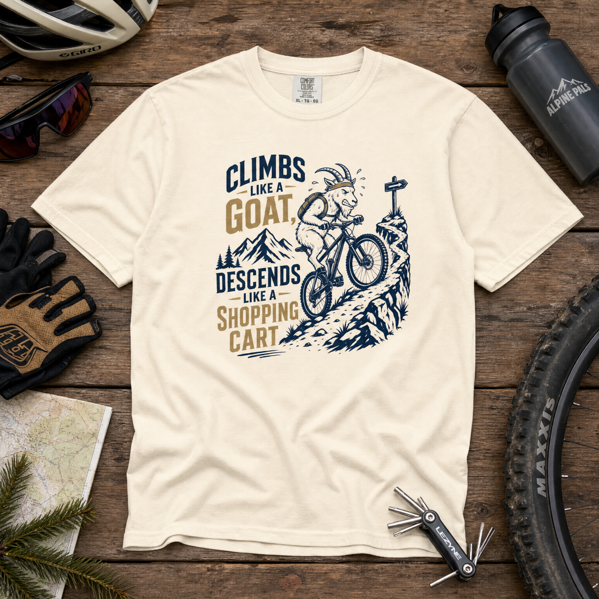 Ivory colored t-shirt with graphic design and text on a wooden surface with cycling accessories.