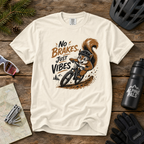 White t-shirt with a graphic of a squirrel riding a bike and 'No Brakes, Just Vibes' text on a wooden surface with cycling accessories.