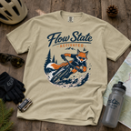 Beige t-shirt with 'Flow State Activated' graphic on a wooden surface with outdoor gear.