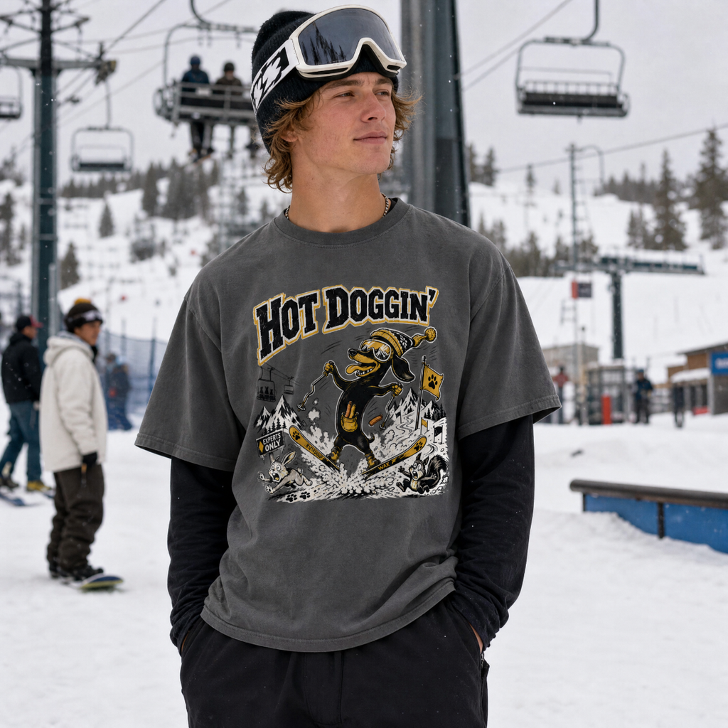 Person wearing a gray t-shirt with 'Hot Doggin' graphic design in a snowy outdoor setting.