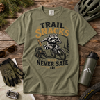 Moss green t-shirt with a raccoon graphic and text on a wooden surface with outdoor accessories.