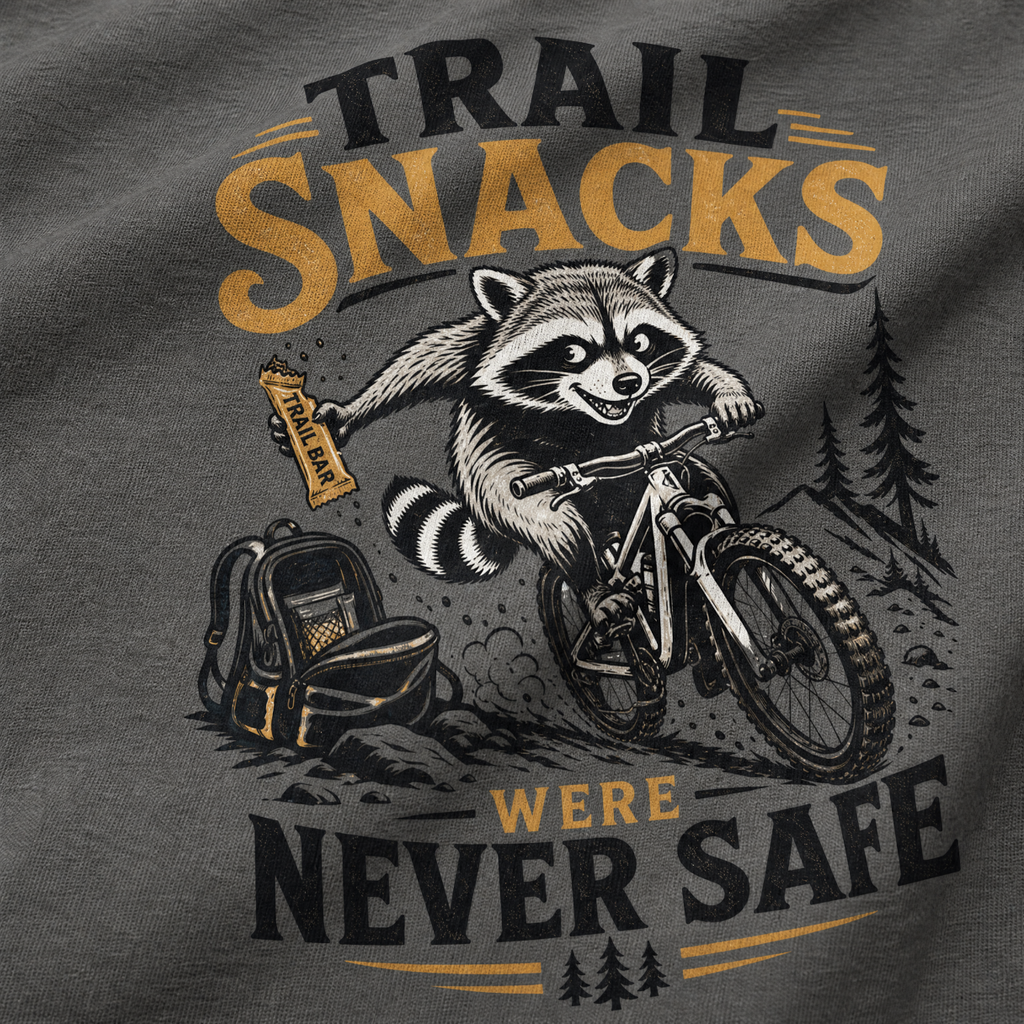 T-shirt with a raccoon riding a bike and holding a snack, text 'Trail Snacks Were Never Safe' on a gray background.