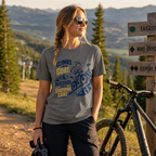Woman with a bicycle standing next to a wooden signpost with mountainous landscape in the background