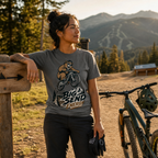 Woman in a mountainous area with a bicycle, wearing a t-shirt with a bear graphic and text.