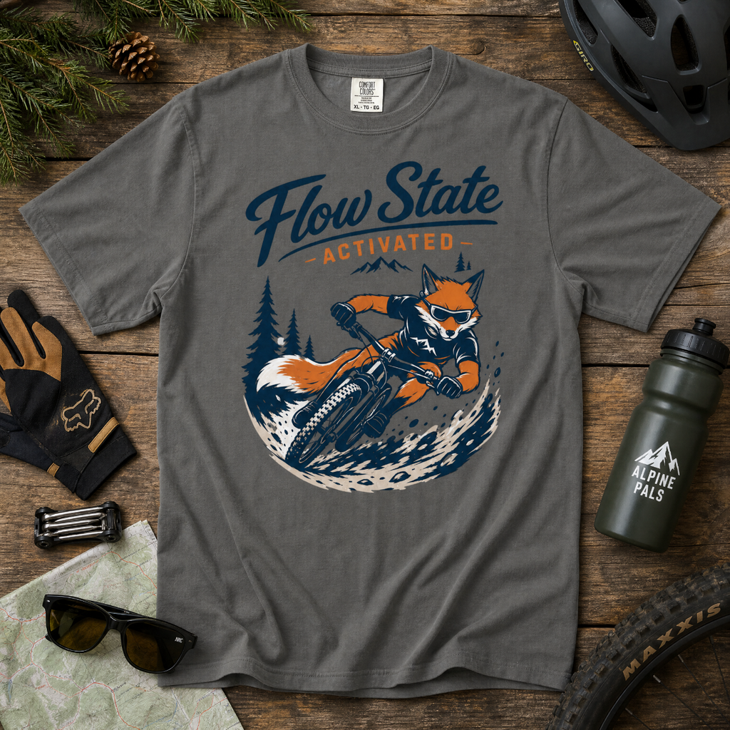 Gray t-shirt with a fox riding a bike graphic and 'Flow State Activated' text on a wooden surface with outdoor gear.