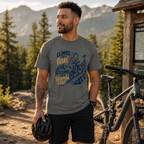 Man wearing a graphic t-shirt standing next to a bicycle with mountains in the background