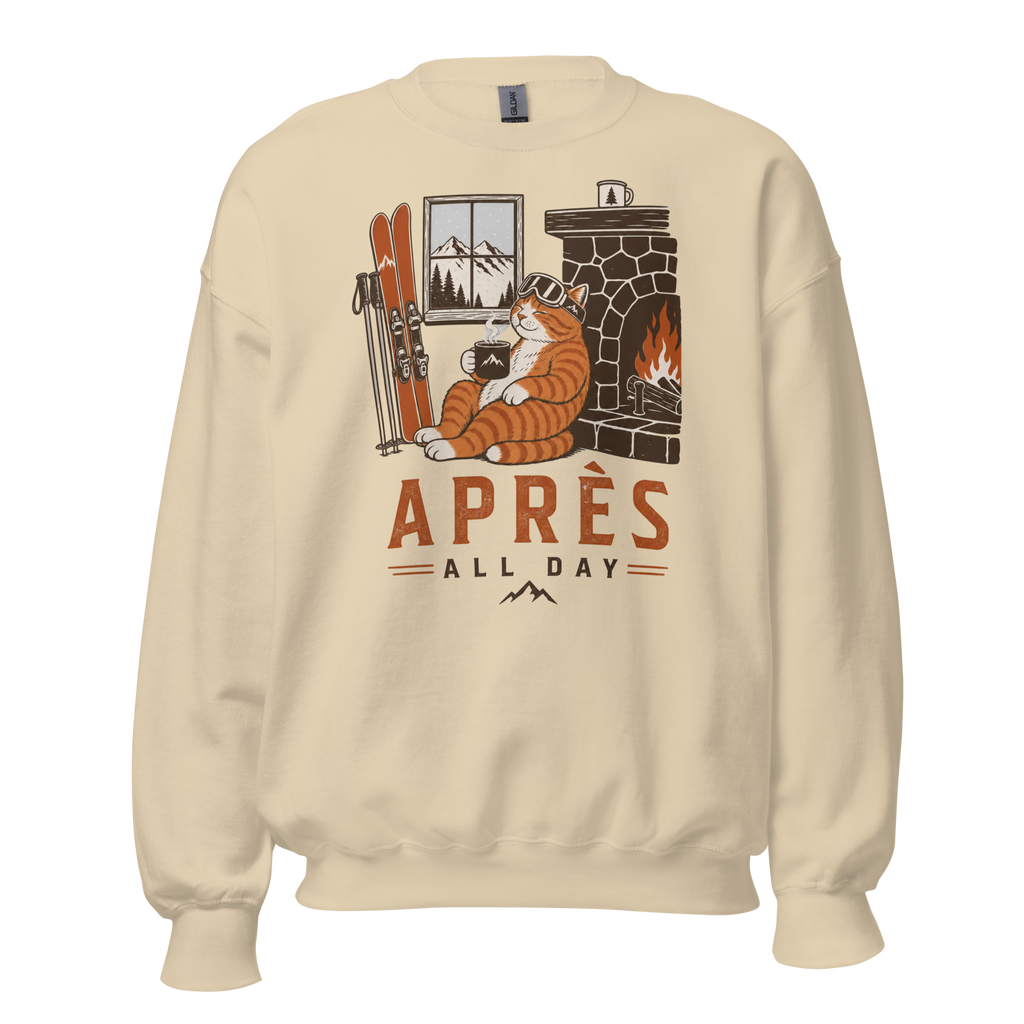 Sand colored sweatshirt with a graphic of a cat by a fireplace and skis, with 'APRES ALL DAY' text.